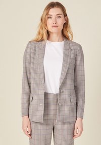 Takkirudu blazer, joka on valmistettu kevyestä kankaasta beige, tummansininen ja burgundy väreissä, jossa on yksittäinen napitus ja viistot kaulukset, yhdistetty valkoisen paidan kanssa.