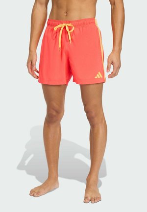 Pantalones cortos de baño naranja brillante con cordón amarillo y franjas laterales. Hechos de material ligero; cuentan con un logo de Adidas en el lado inferior izquierdo.