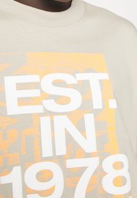 Light gray t-shirt featuring bold white text "EST. IN 1978" overlaying an orange graphic design, with a classic crew neck and soft texture.
