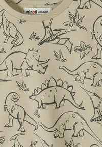 Beżowa dziecięca koszula z czarnymi rysunkami linii przedstawiającymi różne dinozaury i prehistoryczne rośliny, w tym T-Rexa, Stegozaura i Triceratopsa.