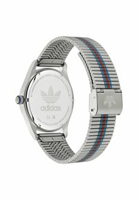 Nerūdijančio plieno laikrodis su sidabriniu tinklo dirželiu, turintis mėlynas ir raudonas juostas. Apvalus korpusas su mėlynu vainiku ir išgraviruotu logotipu ant nugarėlės.