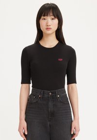 Bodysuit noir à manches courtes en tissu doux avec un col rond et un petit logo rouge Levi's sur la poitrine, associé à un jean foncé taille haute.