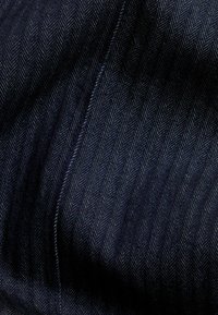 Marinblå herringbone-tyg med en strukturerad väv, som har subtil ribbstruktur och en slät yta. Sömmar sydda längs kanterna.