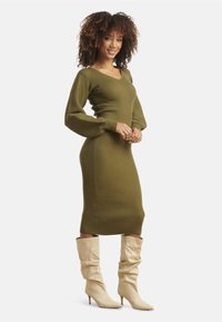 Olive green ribbed knit dress with a V-neck, fitted silhouette, and long puff sleeves, paired with slouchy cream knee-high boots.