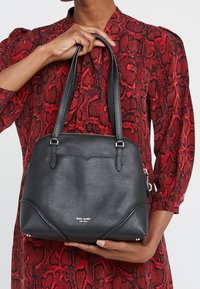 Sort lædertaske med struktureret overflade, dobbelte håndtag, lynlåslukning og sølvfarvede detaljer. Har karakteristisk syning og et mærket logo.