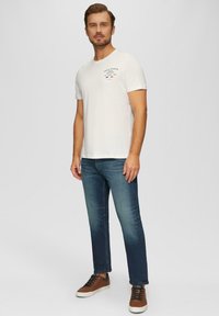 T-shirt en coton blanc à manches courtes avec un petit graphique. Associé à un jean bleu foncé et des baskets basses marron.