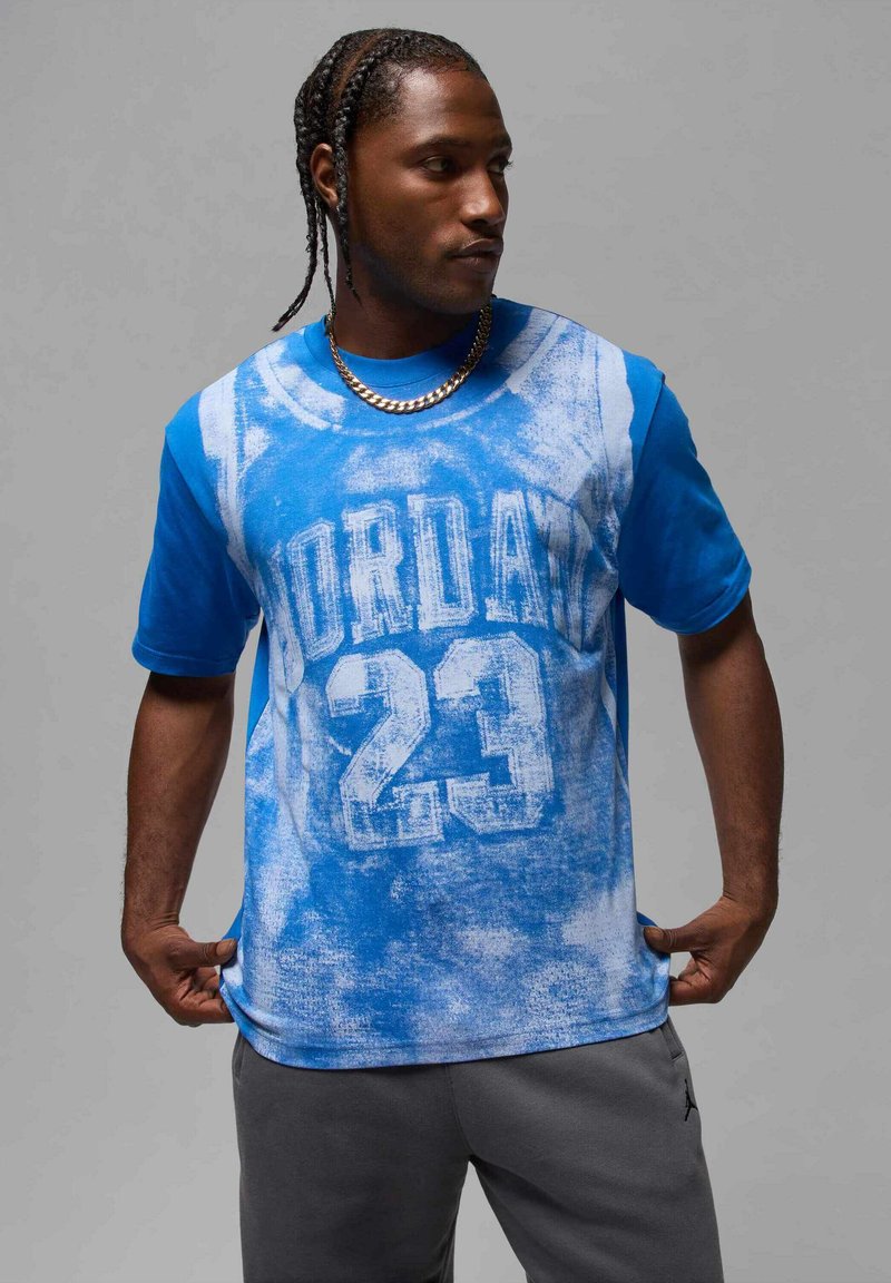 Maglietta blu con grafica sbiadita che presenta "JORDAN" e "23" in bianco. Realizzata in tessuto morbido, maniche corte, vestibilità rilassata.