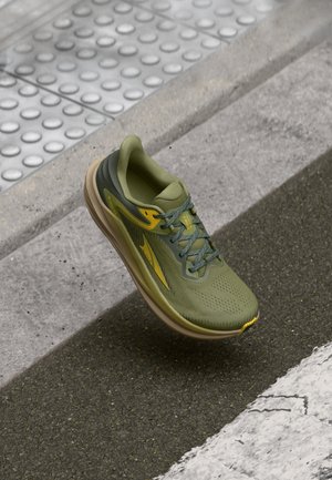 Green running shoe with a mesh upper, textured design, yellow accents, and a cushioned sole. Features laces and a rounded toe shape.