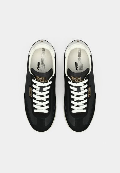 Čierne športové topánky s bielymi šnúrkami a gumovými podrážkami. Majú zlaté logo a hladkú textúru na vrchnej časti materiálu.