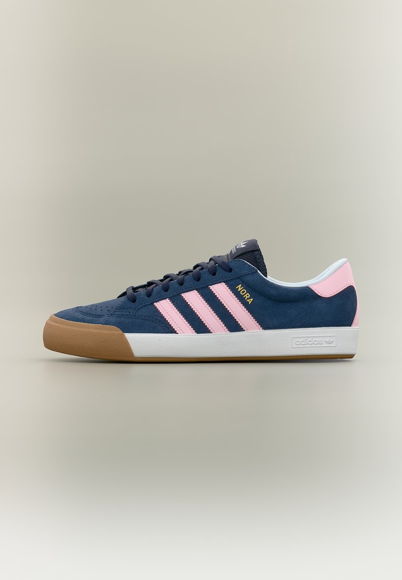 Σκούρο μπλε αθλητικό παπούτσι Adidas με ροζ ρίγες, σόλα από καουτσούκ, λευκό μεσαίο μέρος και τη λέξη «NORA» σε χρυσά γράμματα στο πλάι.