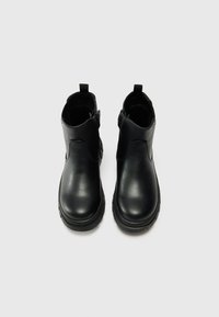 Sorte ankelboots i svart skinn med en glatt overflate, runde tåspisser og elastiske sidepaneler. Har drahåndtak og teksturerte gummisåler.