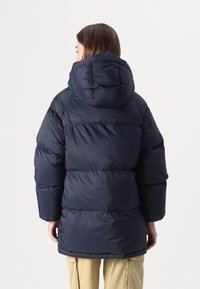 Puffjacka i mörk marin, med huva, oversized silhuett, quiltad design med horisontella sektioner och elastiska ärmslut.