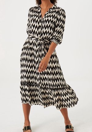 Black and white zigzag patterned dress with a button-up front, short puffed sleeves, and a cinched waist, featuring a flowing hemline.