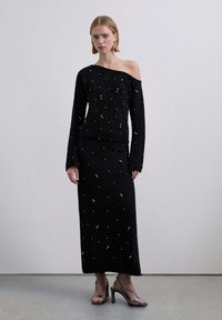 Conjunto de dos piezas de punto negro que incluye un top de hombros descubiertos con mangas largas y una falda larga hasta el suelo, adornados con pequeños detalles plateados esparcidos.