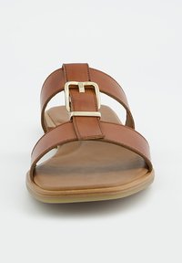 Sandale en cuir marron avec deux brides croisées sur le pied et une boucle dorée sur la bride supérieure, semelle plate, vue de face.