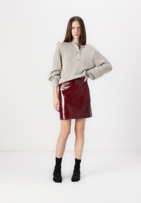 Šedý pletený svetr se třemi knoflíky, doplněný lesklou červenou mini sukní. Černé kotníkové ponožky a minimalistické černé boty dotvářejí vzhled.