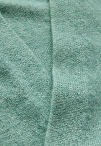 Tissu tricoté vert clair avec une texture douce, présentant une couture diagonale et des nuances variées, mettant en valeur sa qualité moelleuse.