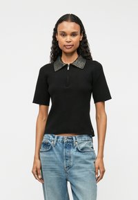 Melna ribota īsām piedurknēm blūze ar rāvējslēdzēja apkakli un uzlīmētām detaļām. Apvienota ar gaiši ziliem džinsiem, izceļot ikdienišķu izskatu.
