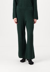 Green knitted pants featuring a ribbed texture and flared design. Paired with black open-toed heels. Accentuates a relaxed fit.