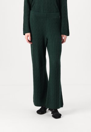 Green knitted pants featuring a ribbed texture and flared design. Paired with black open-toed heels. Accentuates a relaxed fit.