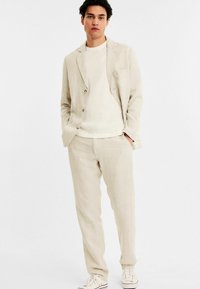Lys beige linned jakkesæt med en enkeltbrystet blazer med to knapper, matchende bukser og en struktureret hvid skjorte under.