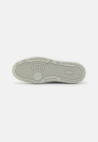 Sole of a sneaker, featuring a textured rubber surface in light gray, with a herringbone pattern and a circular accent in the center.