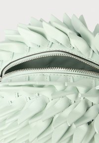 Mala de couro verde-menta com exterior texturizado e detalhes pontiagudos, fecho superior com zíper e forro interior liso.