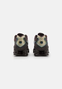 Black athletic shoes with a textured fabric upper, featuring a unique curved heel design, light blue accents, and visible cushioning pods.