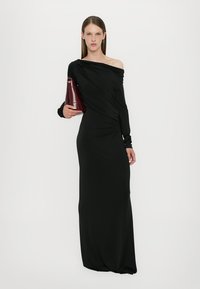 Black, long-sleeve, one-shoulder dress with draped fabric design. Model holds a burgundy handbag. Smooth texture, fitted silhouette.