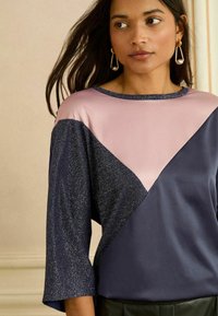 Hosszú ujjú felső színblokk mintával, tengerészkék, rózsaszín és csillogó részletekkel; puha anyag, kerek nyakkivágással és laza szabással.