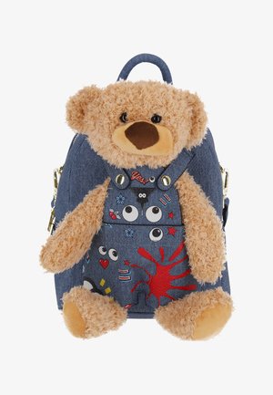 Teddybeer met lichtbruin bont bevestigd aan een blauwe denimrugzak versierd met kleurrijke cartoonogen, sterren, harten en een rood spatterdetail.
