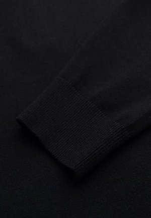 Nahaufnahme eines schwarzen Pulloverelements, das ein geripptes Bündchen und eine glatte Textur aufweist, aus Strickstoff gefertigt für Wärme und Komfort.