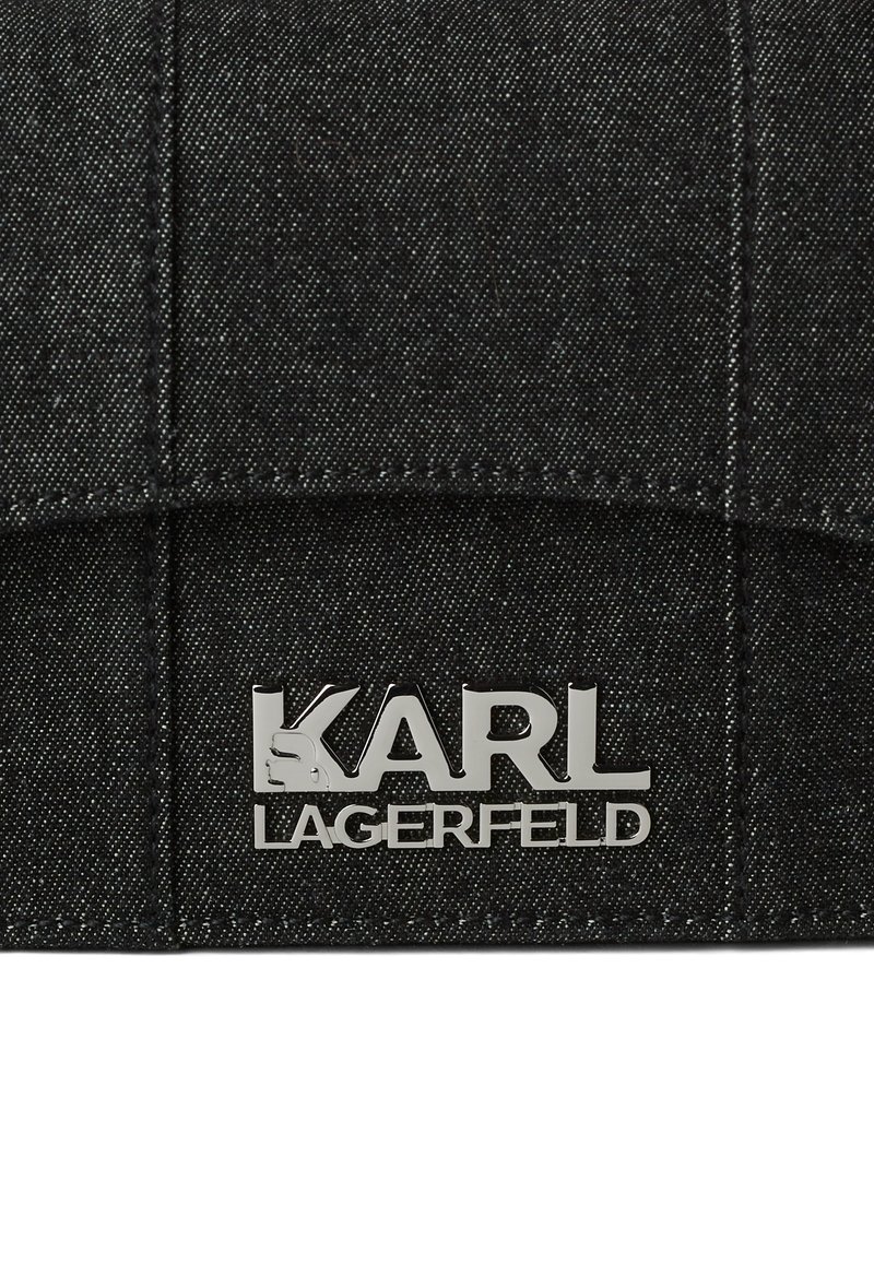 Tissu en denim noir avec des coutures surpiquées et une étiquette en métal argenté portant l'inscription "KARL LAGERFELD" attachée au centre en bas.