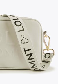 Piccola borsa a tracolla rettangolare beige con strap regolabile, caratterizzata da testo nero "MNT & LOL" e chiusura in metallo dorato.