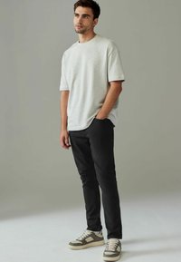 T-shirt gris clair à manches courtes associé à un pantalon slim noir et des baskets beiges avec des accents gris. Design simple et décontracté.