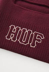 Bordeaux strikket lue med ribbestruktur og hvit brodert "HUF"-logo i tykk skrift, med et utskjært håndtak på toppen.