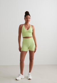 Lichtgroene sportieve crop top met een V-hals en bijpassende high-waisted shorts, gemaakt van een gladde, rekbare stof. Witte sneakers.