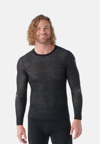 Camisa de base de manga larga negra con un ajuste slim, hecha de un tejido ligero y texturizado, con detalles de malla en las mangas.