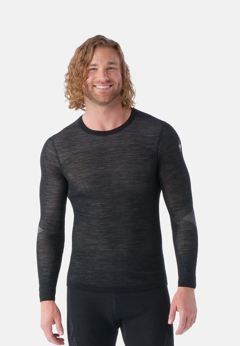 Camisa de base de manga larga negra con un ajuste slim, hecha de un tejido ligero y texturizado, con detalles de malla en las mangas.