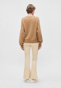 Beige Strickpullover mit puffigen Ärmeln, geripptem Saum und Rundhalsausschnitt, kombiniert mit cremefarbenen, ausgestellten Hosen und weißen Sneakers. Rückansicht.