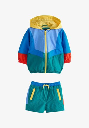 Børns to-delte sæt med gul hættejakke med lynlås i blå, grønblå og røde blokke, parret med grønblå shorts med gul snor og lommer.