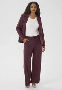 Mauve suit jacket over a white top, paired with matching drawstring trousers. The fabric appears smooth and slightly stretchy.