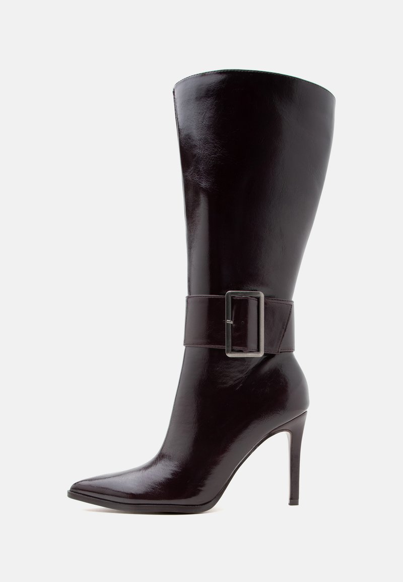 Botte haute en cuir marron foncé à talon haut, bout pointu, avec une large sangle dotée d'une grande boucle métallique rectangulaire autour de la cheville.