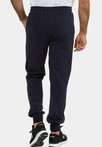 Dunkelblaue Sweatpants mit einem elastischen Bund und Bündchen, aus einem weichen Stoff gefertigt. Dazu werden schwarze Sportschuhe getragen.
