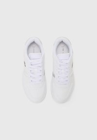 Hvite sneakers med en glatt lærfinish. Funksjoner inkluderer rund tå, forsterket søm og snøring. Lacoste-logo på siden.