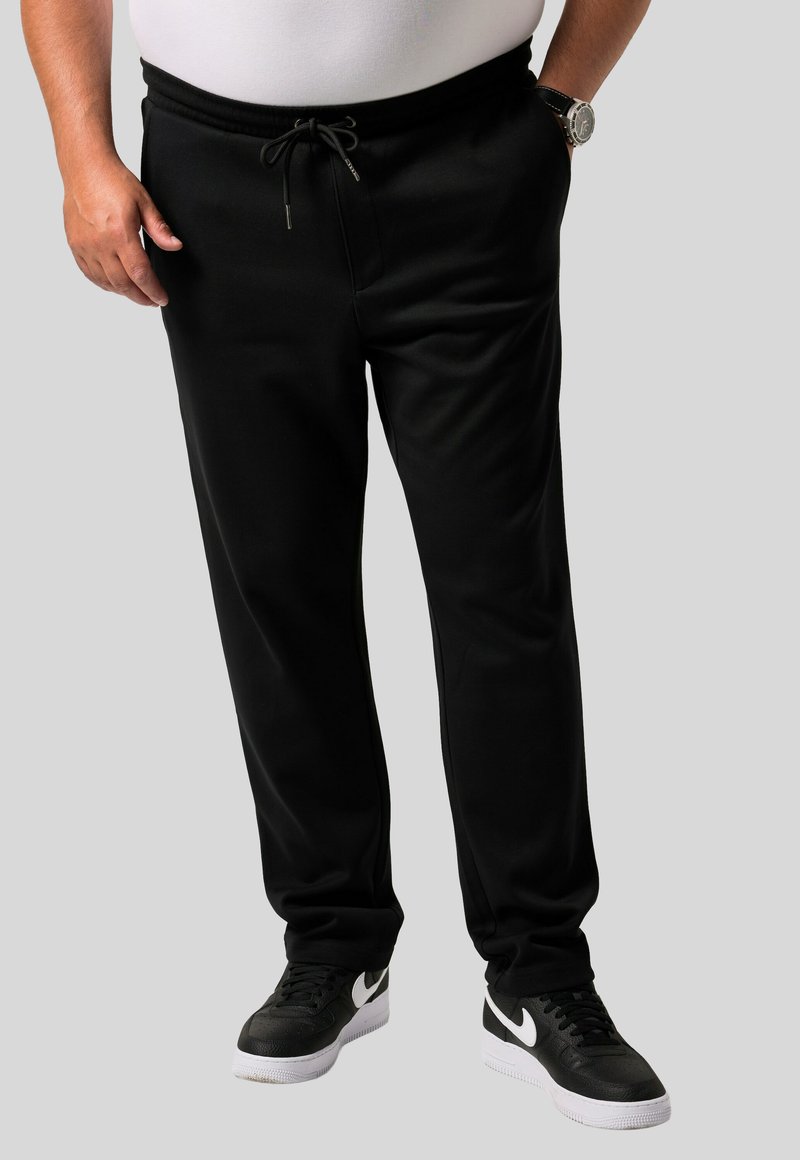 Pantalones de chándal negros de tela suave, con cintura elástica y cordón, y bolsillos laterales, combinados con zapatillas negras.
