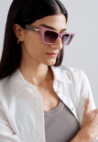 Pink oversized sunglasses with square frames, gradient tinted lenses, and gold accents on the temples, paired with a white button-up shirt.