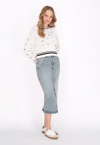 Pulover alb tricotat cu broderie florală și dungă neagră la tiv, asortat cu o fustă din denim bleu deschis și adidași albi.