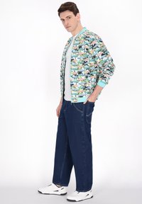 Giubbotto bomber con una stampa multicolore di animali e fogliame, polsini e colletto a coste blu chiaro, abbinato a jeans a gamba larga blu navy e sneakers bianche.