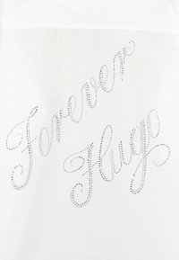 Tessuto bianco con rhinestones scintillanti disposti in una scritta corsiva che dice "Forever Hugo." Texture liscia, design dettagliato.